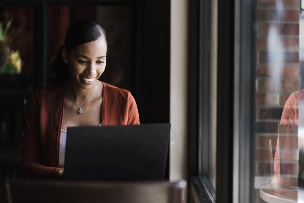 A woman of color smiles at her laptop